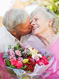 Husband giving wife flowers outdoors kissing and smiling