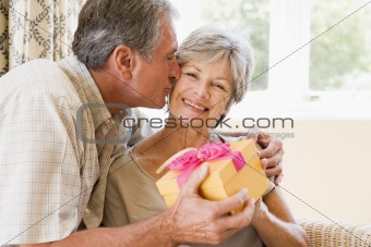 Husband giving wife gift in living room kissing her and smiling