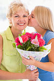 Granddaughter kissing grandmother on cheek holding flowers and s