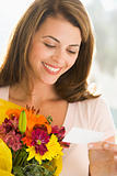 Woman holding flowers and reading note smiling