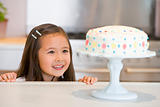 Young girl at kitchen counter looking at cake smiling