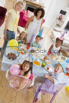 Young children at party with mothers sitting at table with food 