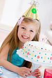 Young girl wearing party hat with birthday cake smiling