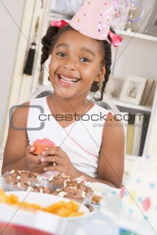 Young girl at party sitting at table with a cupcake smiling