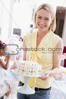 Woman at party holding birthday cake smiling