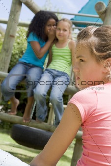 Two young girl friends at a playground whispering about other gi