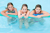 Three young girl friends in swimming pool with pool noodle smili