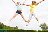 Two young girls jumping on trampoline smiling