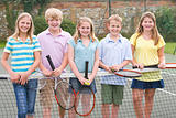 Five young friends with rackets on tennis court smiling