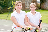 Two young girl friends with rackets on tennis court smiling