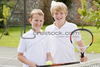 Two young male friends with rackets on tennis court smiling