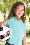 Young girl holding soccer ball outdoors smiling