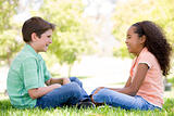 Tow young friends sitting outdoors looking at each other and smi