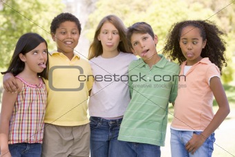 Five young friends standing outdoors making funny faces