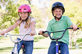 Brother and sister outdoors on bicycles smiling