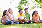 Five young friends sitting outdoors with soccer ball looking up