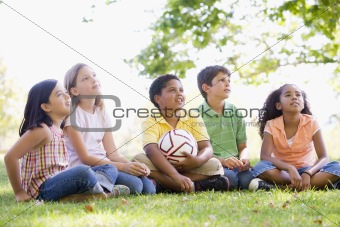 Five young friends sitting outdoors with soccer ball looking up