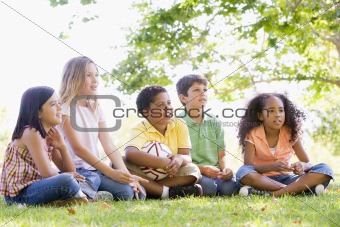 Five young friends sitting outdoors with soccer ball
