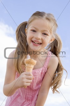 Young girl outdoors eating ice cream cone and smiling