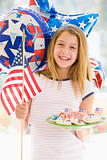 Young girl outdoors on fourth of July with flag and cookies smil
