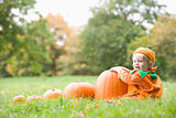 Baby boy outdoors in pumpkin costume with real pumpkins