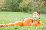 Baby boy outdoors in pumpkin costume with real pumpkins