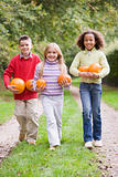 Three young friends walking on path with pumpkins smiling