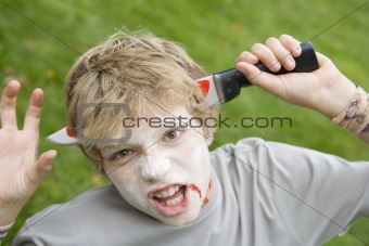 Young boy with scary Halloween make up and plastic knife through