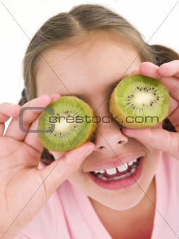 Young girl holding kiwi halves over eyes smiling
