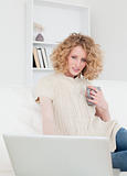 Cute blonde woman relaxing with her laptop while sitting on a so