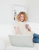 Lovely blonde woman relaxing with her laptop while sitting on a 