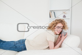 Good looking blonde woman enjoying a cup of coffee while lying o