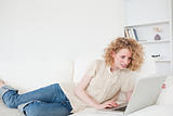 Pretty blonde woman relaxing with her laptop while lying on a so
