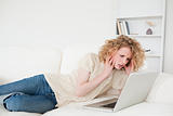 Gorgeous blonde woman relaxing with her laptop while lying on a 