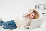 Attractive blonde woman relaxing with her laptop while lying on 