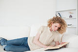 Beautiful blonde woman reading a book while lying on a sofa