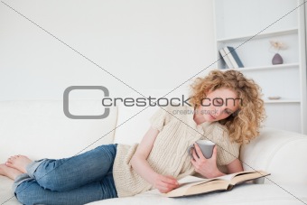 Pretty blonde woman reading a book and holding a cup of coffee w