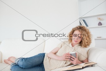 Beautiful blonde woman reading a book and holding a cup of coffe