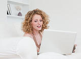 Smiling blonde female relaxing with her laptop while sitting on 