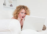 Attractive surprised female relaxing with her laptop while sitti