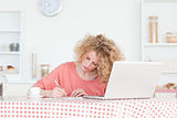 Beautiful blonde woman writing while working with her laptop in 