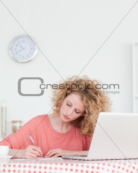 Attractive blonde woman writing while working with her laptop in
