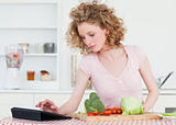 Pretty blonde woman relaxing with her tablet while cooking some 