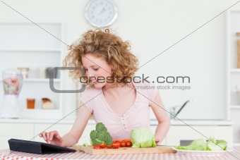 Beautiful blonde woman relaxing with her tablet while cooking so