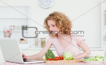 Pretty blonde woman relaxing with her laptop while cooking some 