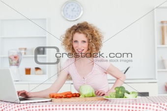 Beautiful blonde woman relaxing with her laptop while cooking so