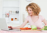 Attractive blonde woman relaxing with her laptop while cooking s