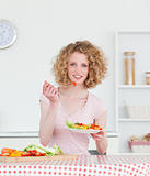 Pretty blonde woman eating some vegetables in the kitchen