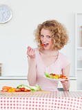 Charming blonde woman eating some vegetables in the kitchen