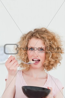 Attractive blonde woman eating a bowl of cereals in the kitchen